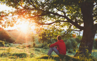 Man sitting outdoor under a tree and admiring the sunrise. Photo by AlexSava/iStockPhoto.com